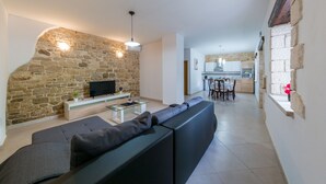 A modern living room with a stone wall, a black sofa, a glass coffee table, and a flat-screen TV. - Stone house Furlani with a lovely garden (Svetvincenat)