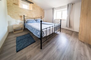 Un dormitorio con pared de piedra, cama con estructura metálica, mesita de noche de madera y ventana con cortinas.