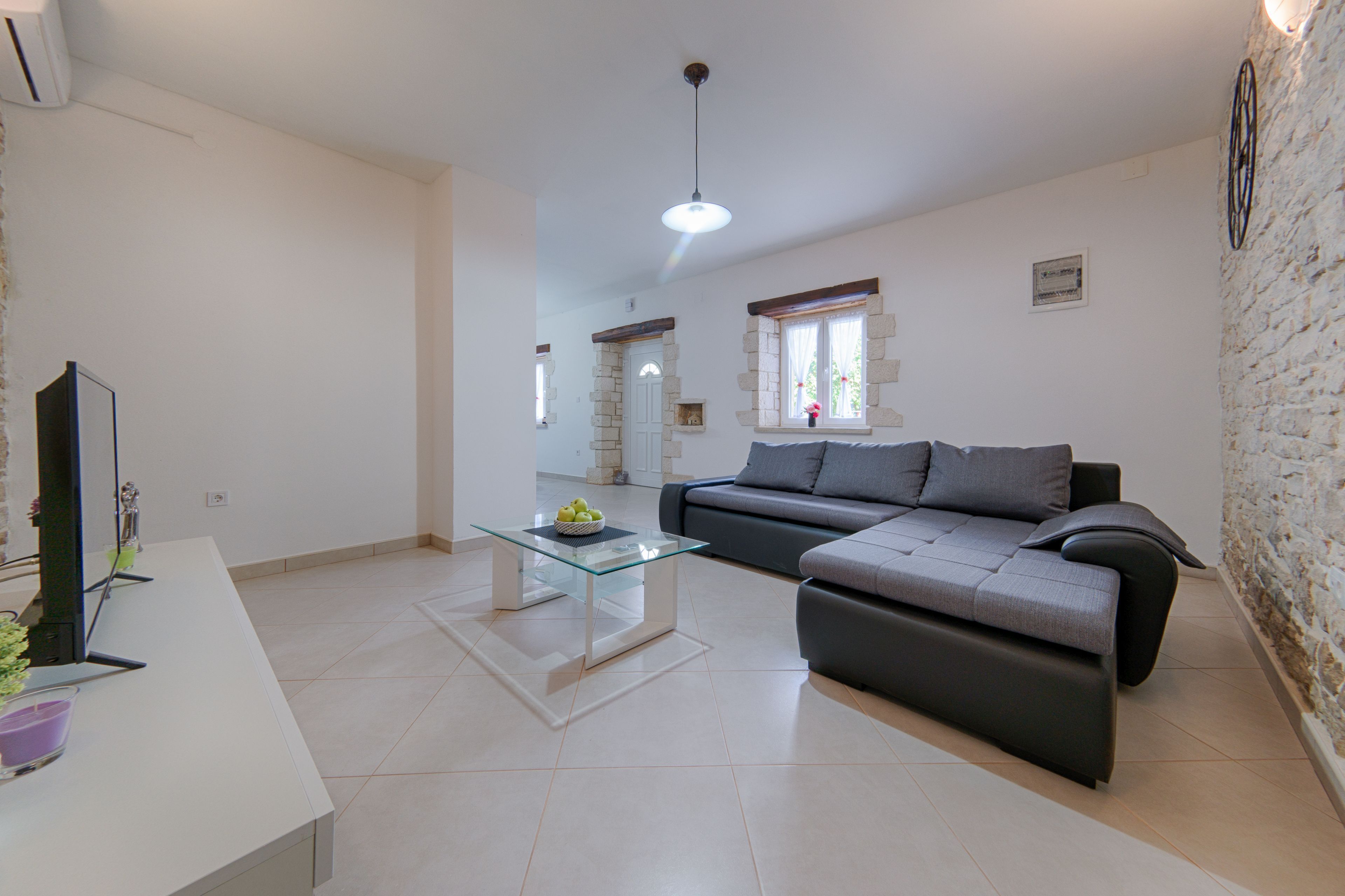 Una sala de estar moderna con una mesa de centro de vidrio, un sofá gris y un televisor sobre un mueble blanco.