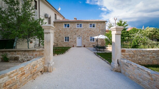 A stone building with a gravel path leading to a white door, surrounded by greenery and a clear sky. - Stone house Furlani with a lovely garden (Svetvincenat)