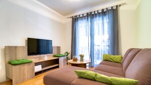 Un salon moderne doté d’un téléviseur à écran plat, d’un meuble de rangement en bois et d’un canapé marron agrémenté de coussins verts.