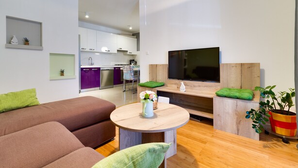 Un salon moderne avec un canapé marron, une table basse ronde en bois et un téléviseur à écran plat fixé à un mur en bois.