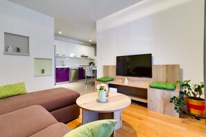 A modern living room with a brown sofa, a round wooden coffee table, and a flat-screen TV mounted on a wooden wall. - Charming and sweet apartment Vito (Pula)