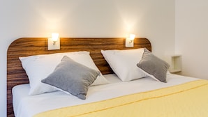 Un lit bien fait, avec une tête de lit en bois, deux oreillers et une table de chevet sur laquelle se trouve une lampe.