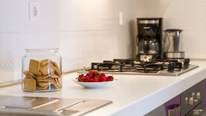 Une cuisine avec un plan de travail blanc, un bocal en verre rempli de biscuits et un saladier de fraises.