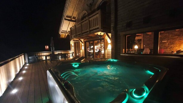 Un bain à remous sur une terrasse en bois, avec un bâtiment en pierre en arrière-plan.