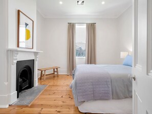 Een slaapkamer met een bed, een open haard, een raam met gordijnen en een klein tafeltje.