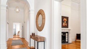 A hallway with wooden flooring, a grey rug, a wooden console table, and a round mirror on the wall.