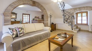 A living room with a white sofa, a patterned throw, and a wooden coffee table. A stone archway and staircase are visible in the background. - Holiday house Matija with a pool (Svetvincenat)