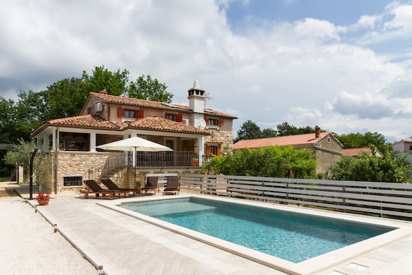 A two-story house with a swimming pool, outdoor furniture, and a white fence.