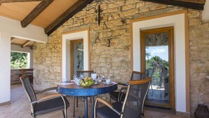 A stone-walled patio with a round table and chairs, a small fruit bowl, and a view of the outdoors. - Holiday house Matija with a pool (Svetvincenat)