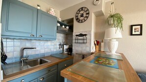 A kitchen with blue cabinets, a sink, a coffee maker, and a clock on the wall. - 2* Apartment with garden, air conditioning, near the pond in Balaruc-les-Bains (Balaruc-les-Bains)