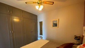 A bedroom with a bed, a wardrobe, a ceiling fan, a bedside table, and a lamp. - 2* Apartment with garden, air conditioning, near the pond in Balaruc-les-Bains (Balaruc-les-Bains)