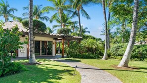 Un resort con un espacio al aire libre cubierto, palmeras y un césped cuidado.