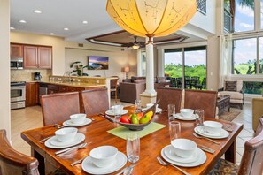 Un comedor amplio con una mesa de madera dispuesta para seis personas, rodeado de asientos cómodos. Un gran ventanal ofrece vistas a exuberante vegetación.