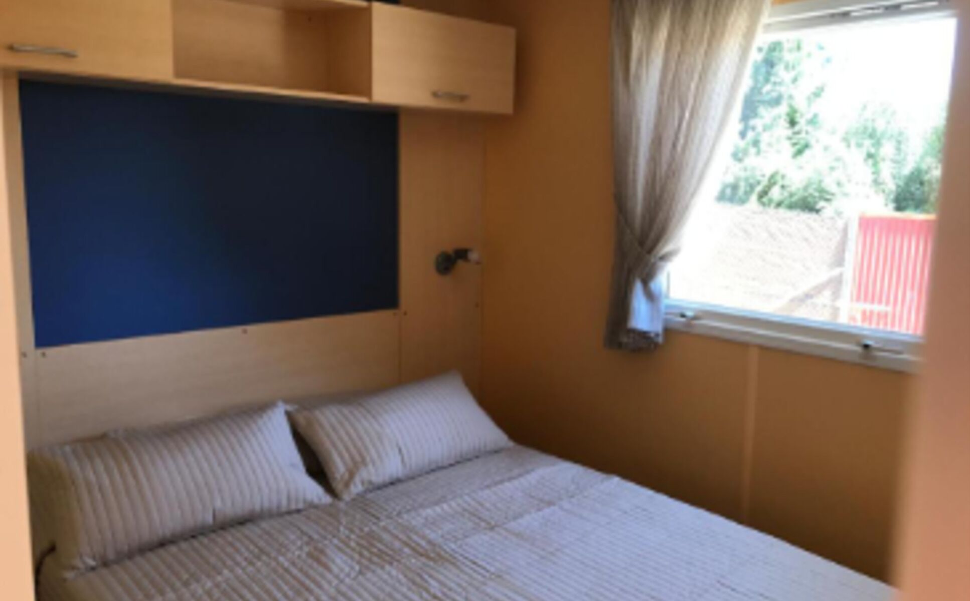 Ein Schlafzimmer mit einem Bett, einem Fenster mit Vorhängen und einem blauen Kopfteil.