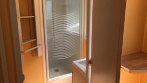 A bathroom with a glass shower enclosure, a wooden door, and a small shelf.