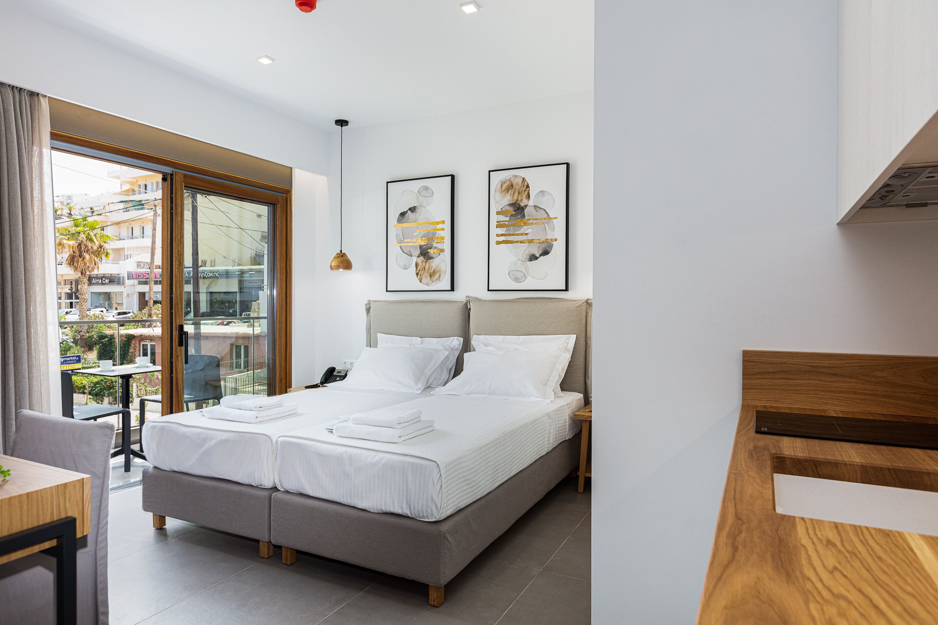 A modern hotel room with a large bed, a desk, and a balcony with a view of the city.