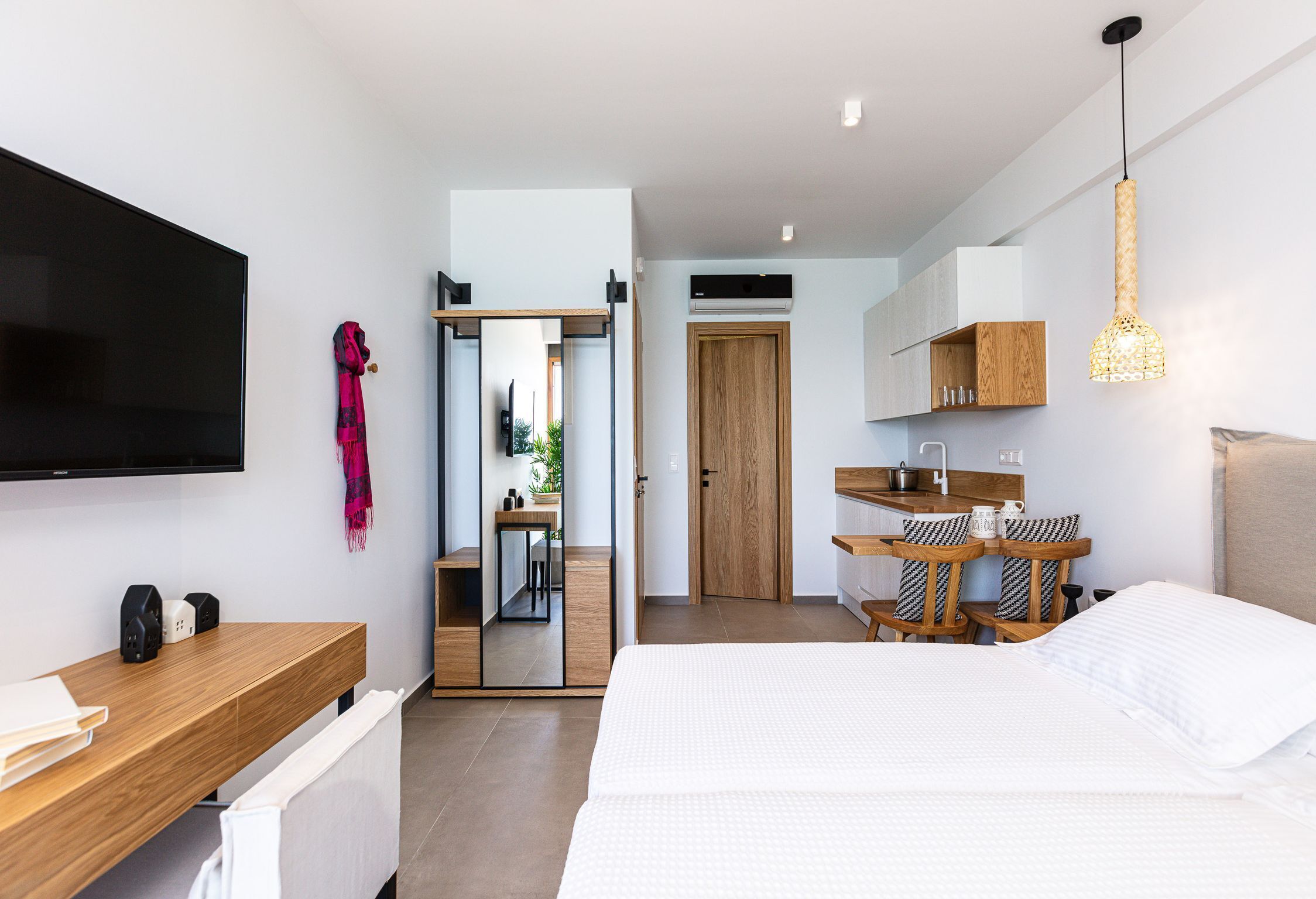 Una habitación de hotel moderna con una cama grande, un escritorio de madera, un televisor de pantalla plana, un espejo y una pequeña kitchenette.