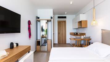 Una habitación de hotel moderna con una cama grande, un escritorio de madera, un televisor de pantalla plana, un espejo y una pequeña kitchenette.