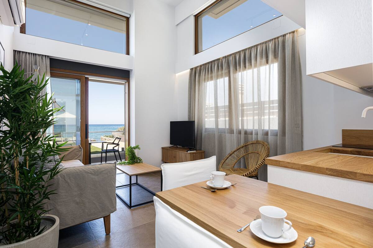 A modern hotel room with a balcony, a dining area, and a kitchen.