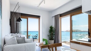 A modern living room with a sofa, dining table, and large windows overlooking the sea. - North Coast Seaside Suites (Rethymno)