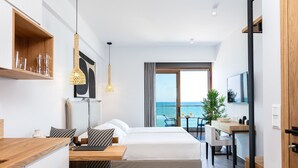 A modern hotel room with a large bed, a wooden desk, a dining area, and a view of the sea. - North Coast Seaside Suites (Rethymno)