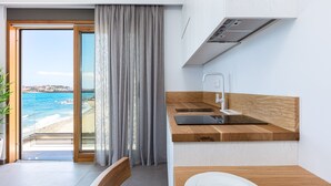 A modern kitchen with a wooden countertop and a view of the beach through a glass door. - North Coast Seaside Suites (Rethymno)