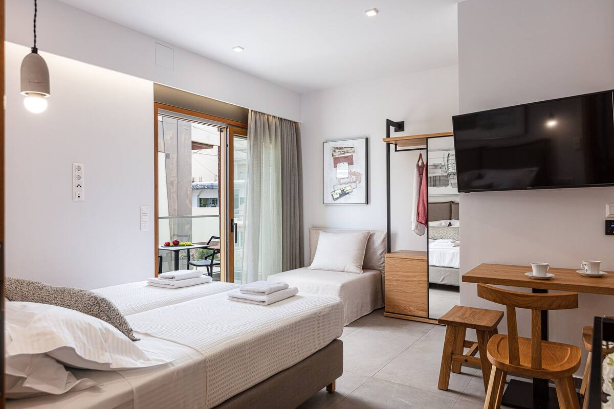 A hotel room with two beds, a TV, a small wooden table with chairs, and a view of the outside.
