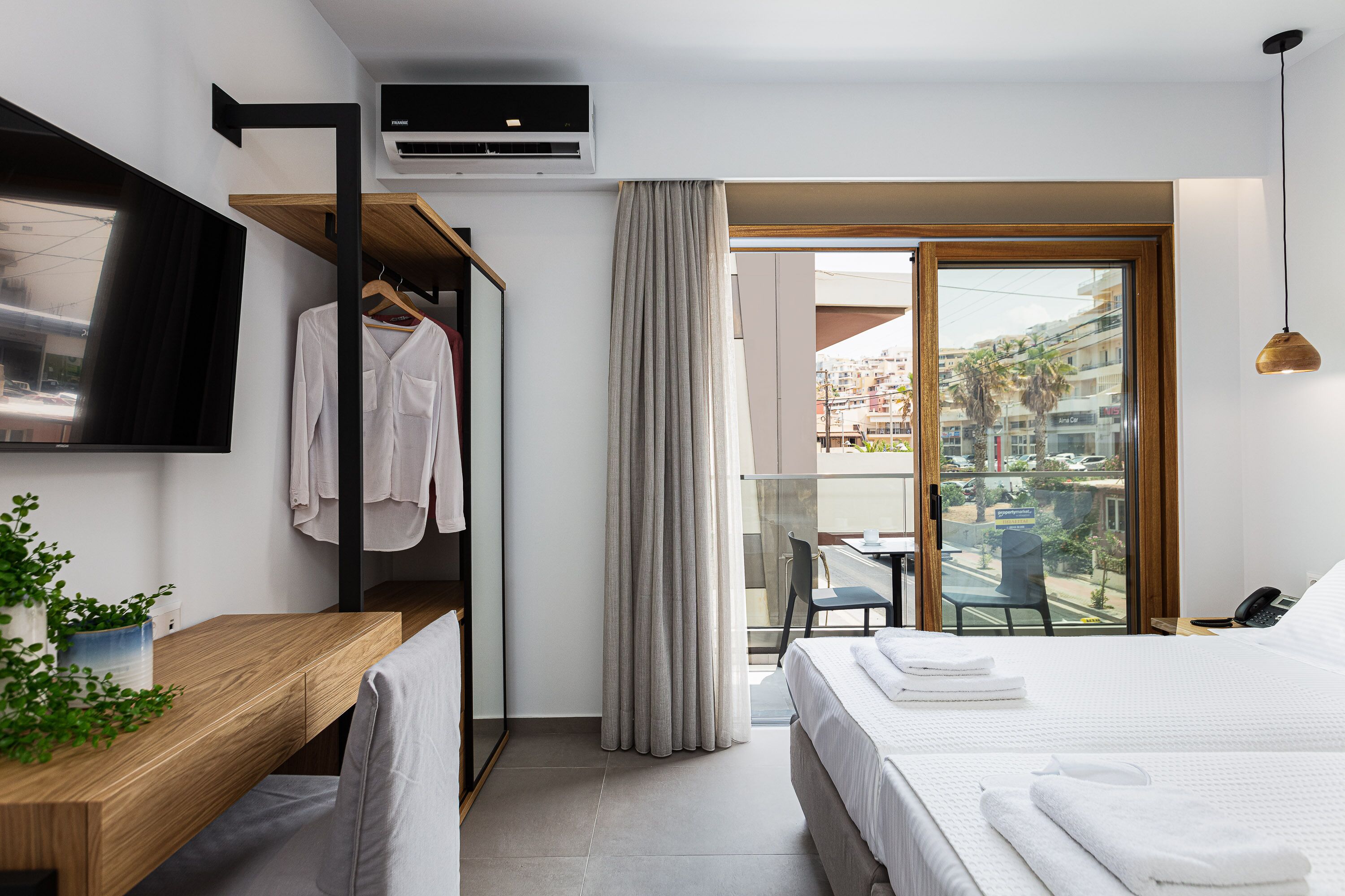 Habitación de hotel moderna con cama, escritorio, televisión, perchero y balcón con vista a la ciudad.