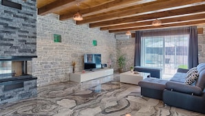 Een moderne woonkamer met een stenen muur, houten balken, een open haard, een televisie en een groot raam.