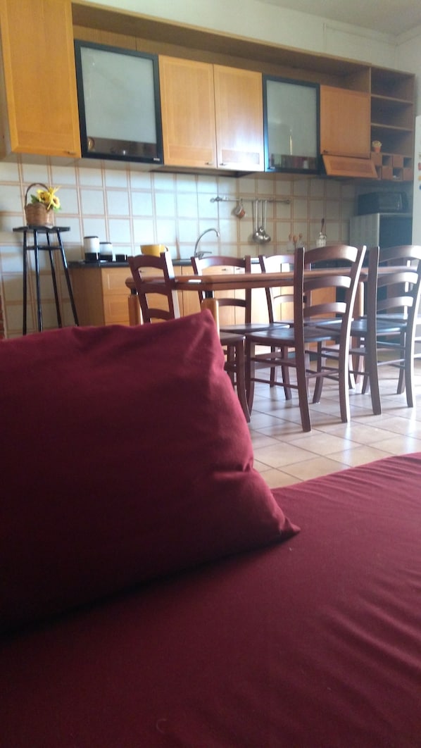 Une cuisine avec des meubles de rangement en bois, une table à manger avec des chaises et un coussin rouge sur le sol.