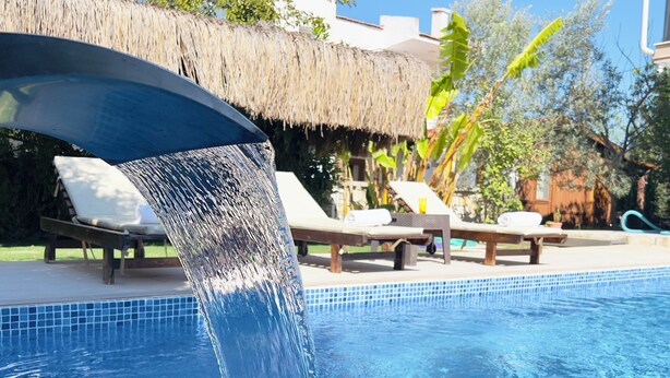A pool with a water feature, lounge chairs, and a thatched roof structure. - Cesmeli Boutique Hotel (Cesme)