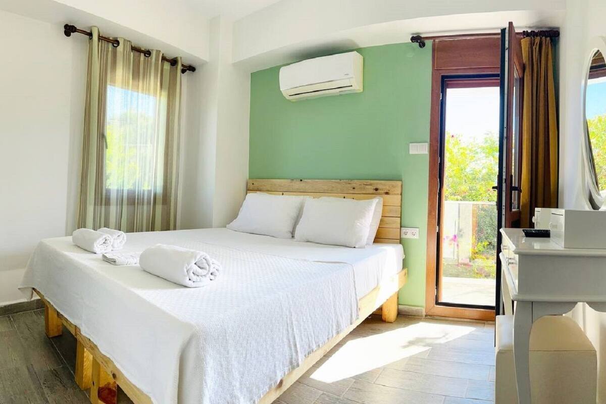 A hotel room with a bed, a wooden headboard, a white bedside table, and an air conditioning unit on the wall.