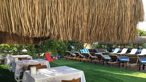 An outdoor dining area with tables and chairs, a poolside lounge area with sun loungers, and a thatched roof overhead. - Cesmeli Boutique Hotel (Cesme)
