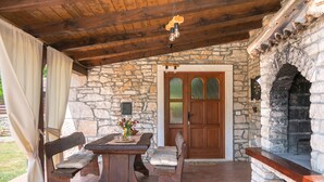 A stone-walled patio with a wooden table and benches, a stone fireplace, and a wooden door with glass panels. - House 1993/28059 (Istria - Rakalj), 900m from the beach (Rakalj)