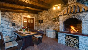 A stone fireplace with a fire, a wooden bench, a table with a vase of flowers, and a stone wall. - House 1993/28059 (Istria - Rakalj), 900m from the beach (Rakalj)