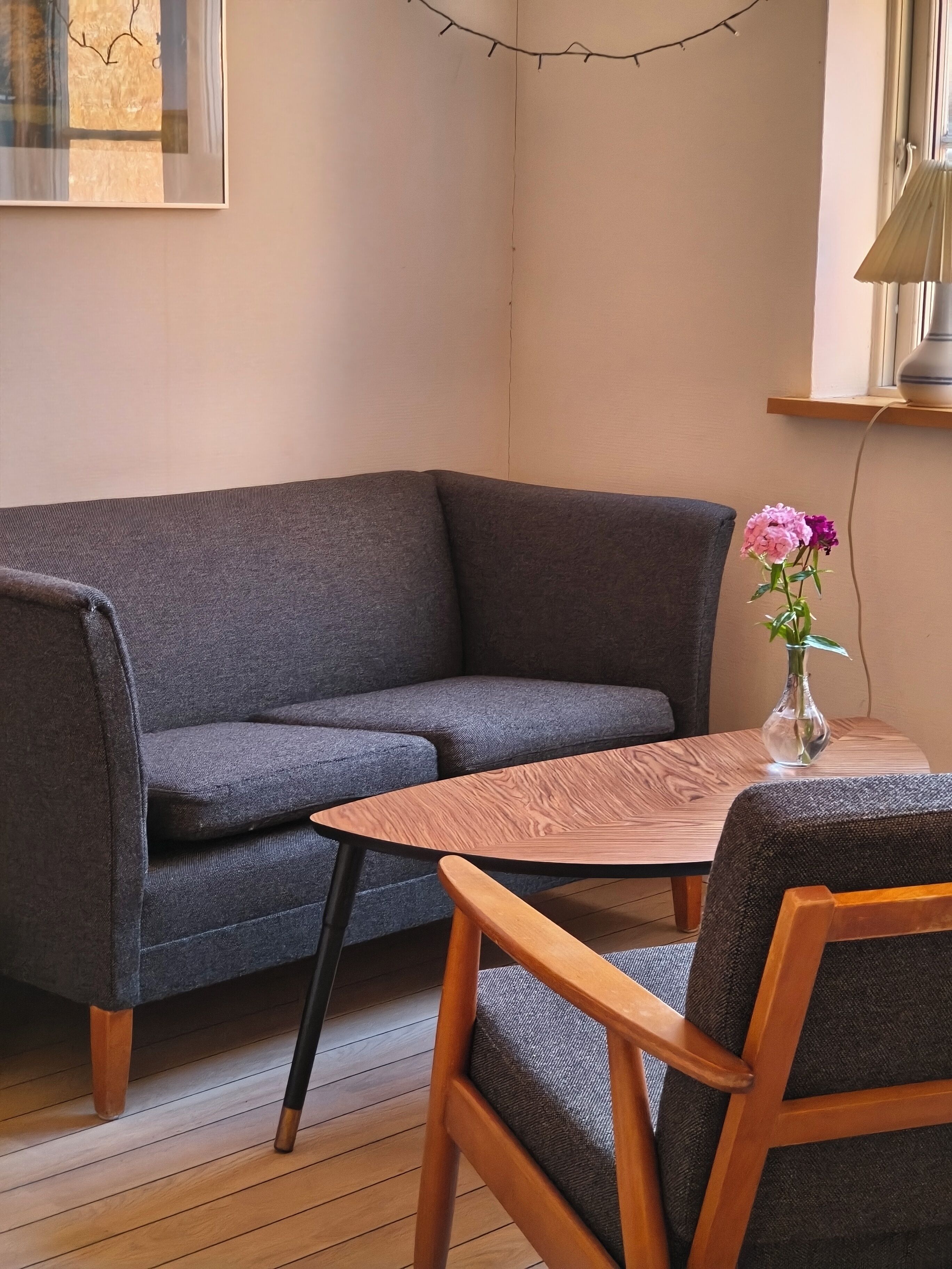 A room with a grey sofa, a wooden table, and a vase with flowers.