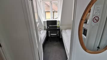 Une petite pièce comprenant un lit, un bureau avec un ordinateur et une fenêtre.