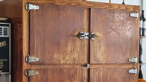 Un mueble de madera con bisagras metálicas y una encimera de madera con una campana de bronce.