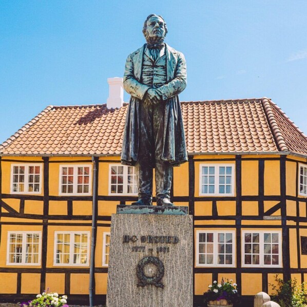 A statue of a man in period clothing, standing on a pedestal with a plaque that reads "L. Orsted 1877-1891". - Hotel Skandinavien (Rudkobing)
