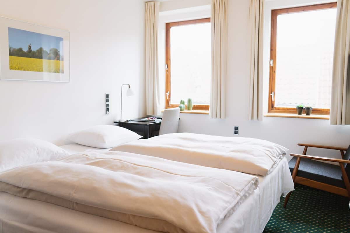 Una habitación de hotel con una cama grande, dos ventanas, un escritorio y una silla.