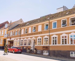 Un edificio con el letrero "SKANDINAVIEN" en la fachada, que presenta un estilo arquitectónico tradicional con marcos de ventanas blancos y tejado de tejas.