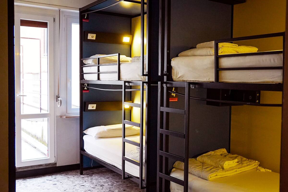 A dormitory room with bunk beds, a door, and a window.