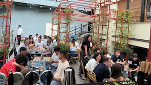 An outdoor seating area with tables and chairs, surrounded by red metal structures and greenery. - YellowSquare Milan (Milan)