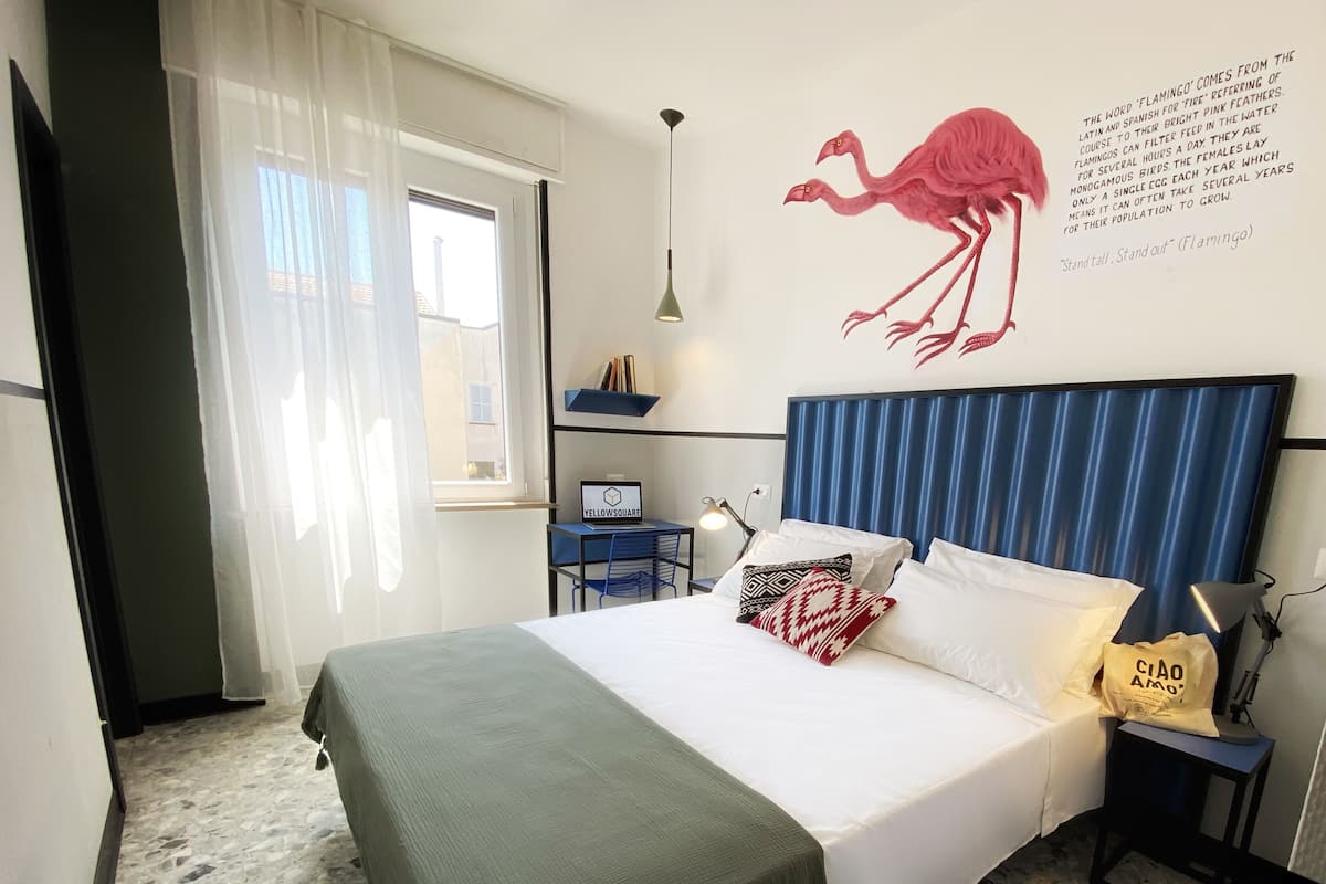 A bedroom with a bed, a desk, a chair, a lamp, and a wall decoration.