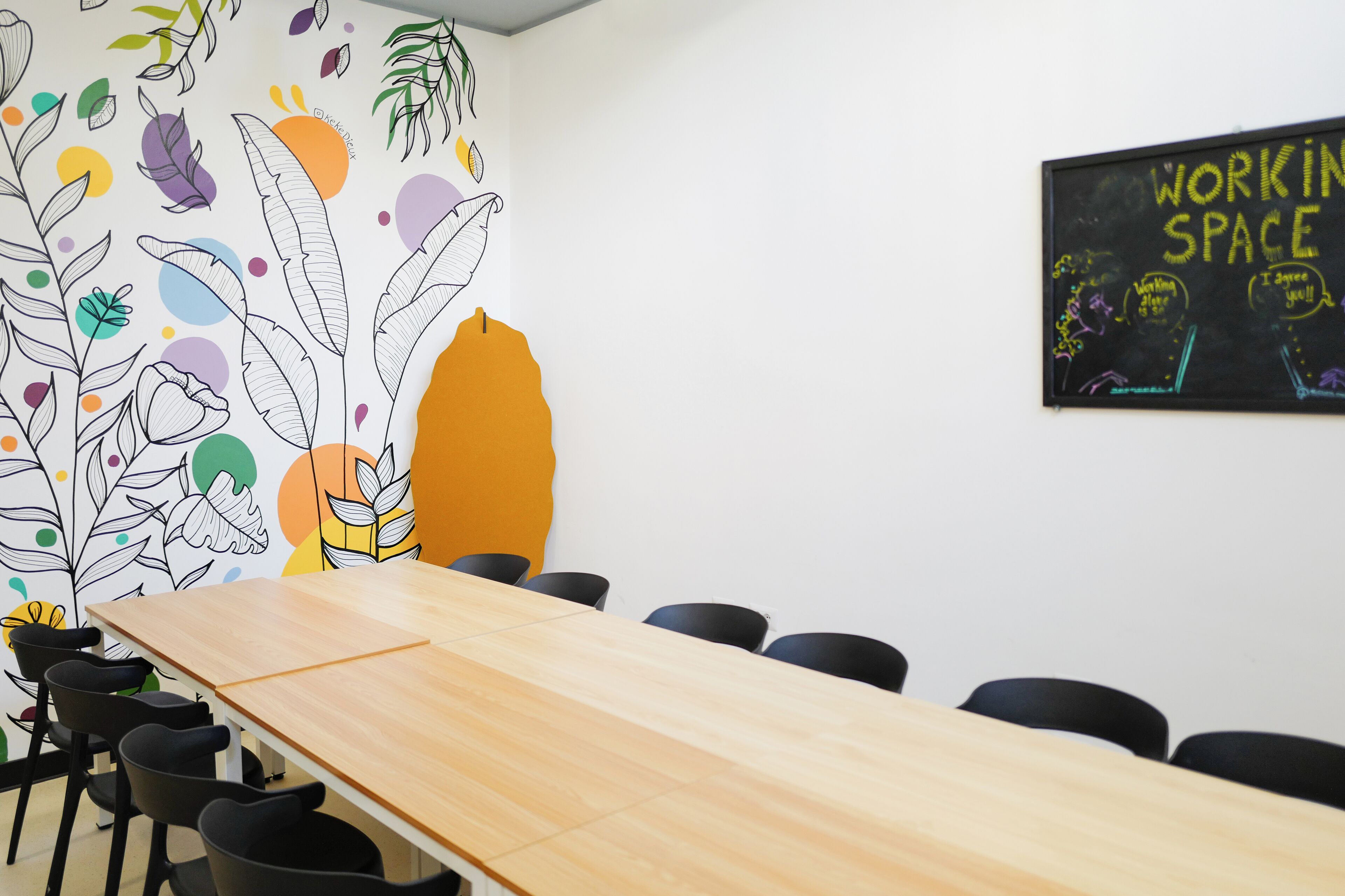 A conference room with a long wooden table, black chairs, and a colorful wall mural.