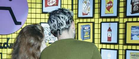 Two people examining framed items on a yellow grid wall.