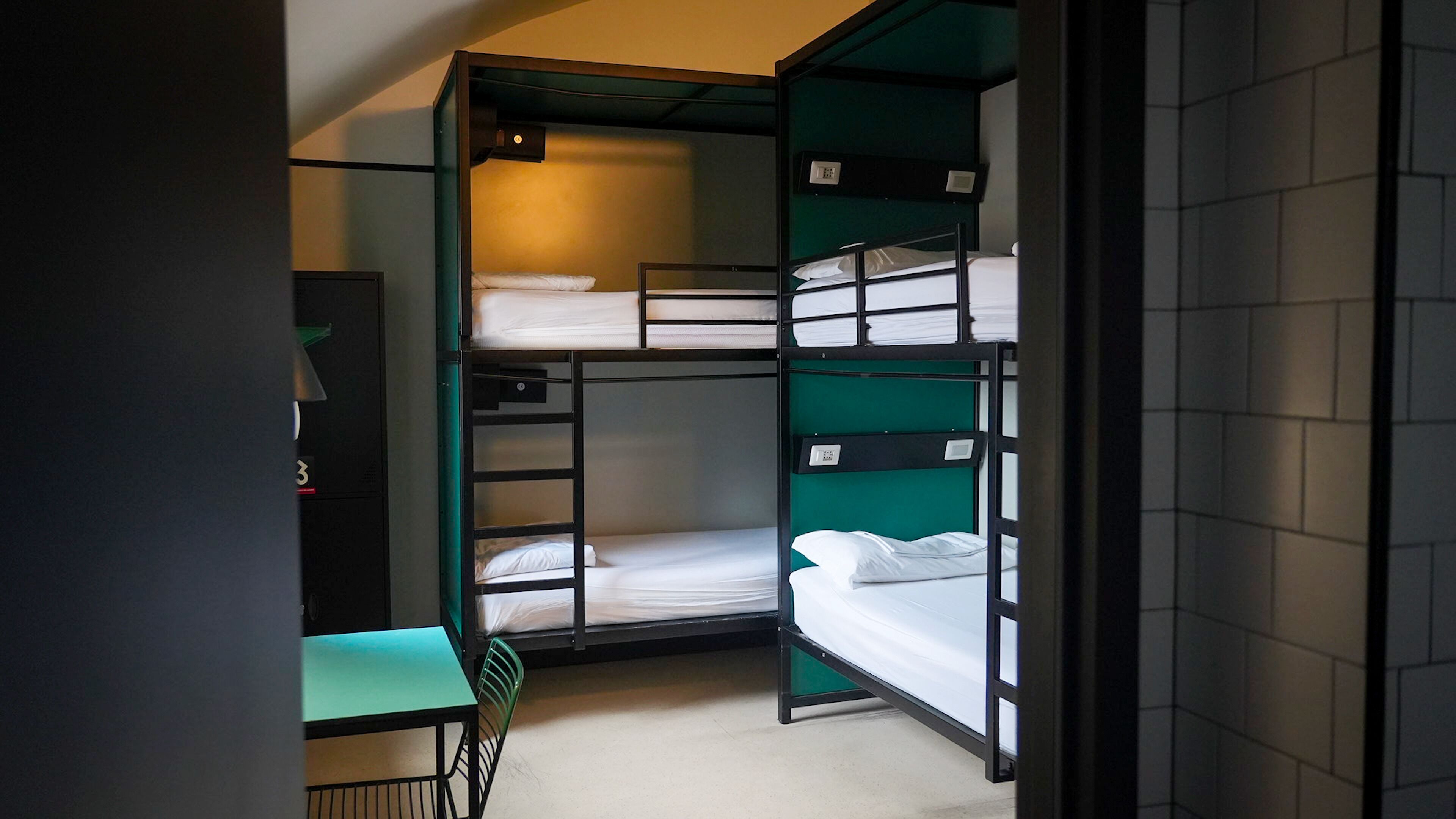 A dormitory room with bunk beds, a desk, and a chair.