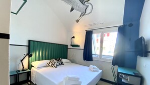 A hotel room with a bed, a desk, a chair, a lamp, a window with curtains, and a wall mural. - YellowSquare Milan (Milan)